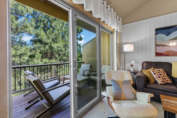 Step into your cozy living room where natural light pours through sliding doors leading to your private balcony. Sink into comfortable seating and enjoy serene forest views framed by towering pines.