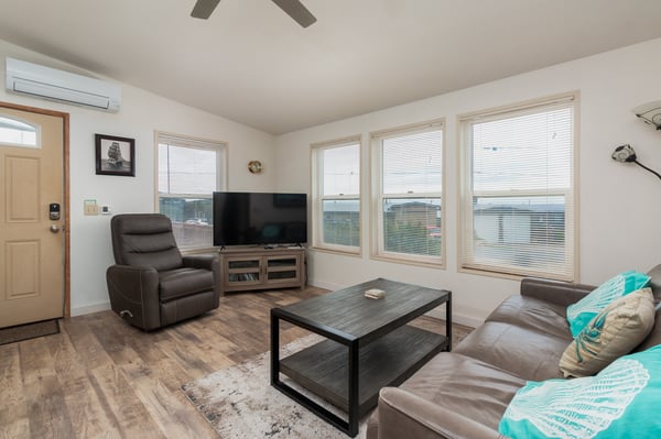 Relax in your bright, airy living room with plush leather seating, a ceiling fan for comfort, and large windows framing peaceful water views just beyond the blinds.