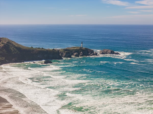 The property is located near a stunning coastal area with turquoise waves, a historic lighthouse, and dramatic rocky headlands marking the shoreline.