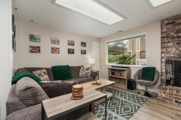 Sink into the plush sofa and feel at home in this sunlit living space with charming skylights, warm wood touches, and a cozy exposed brick fireplace calling you to unwind.