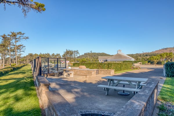 Expansive outdoor patio with picnic table and fire pit surrounded by lush lawns and forested hills.