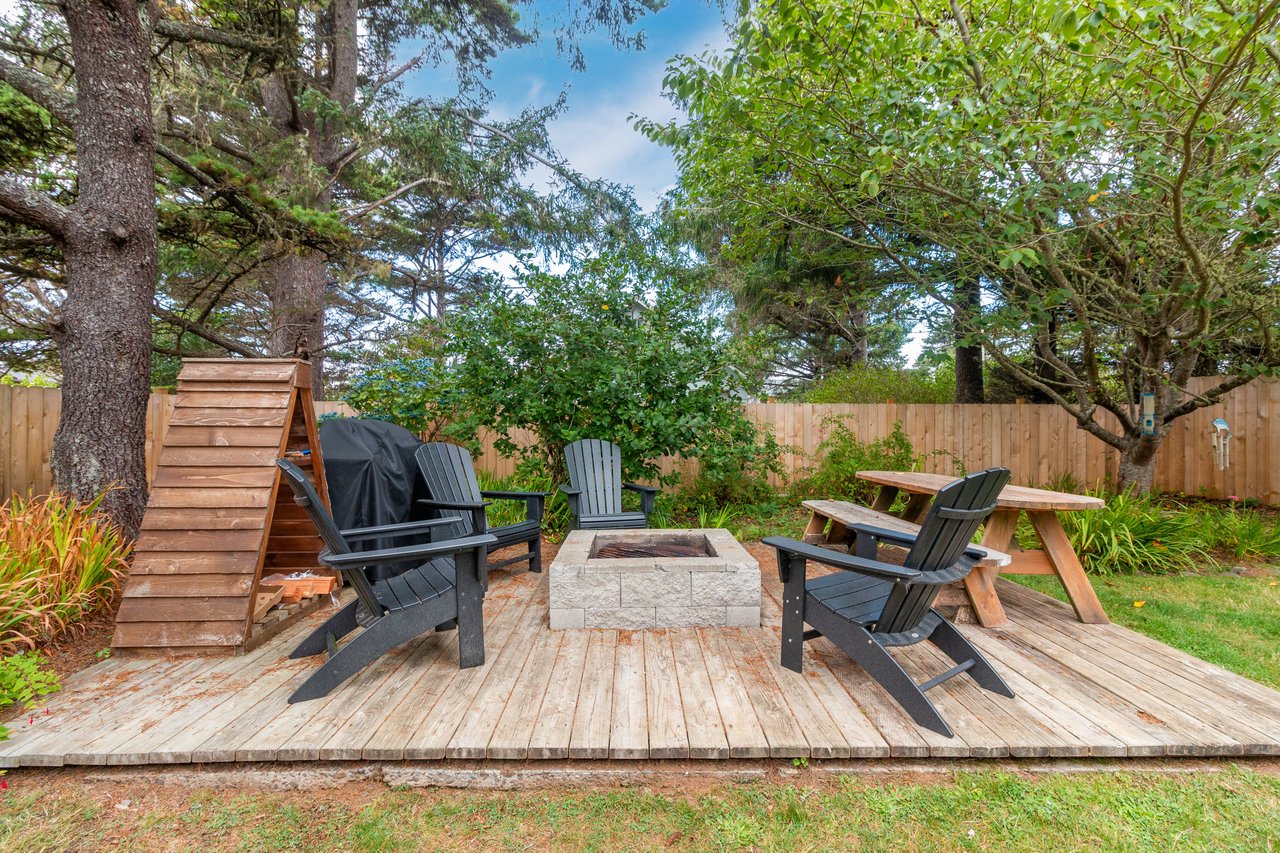 A private backyard retreat with fire pit seating and towering pines, offering a peaceful spot to unwind under open sky and surrounded by natural greenery.