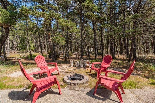 Gather around the stone fire pit in your private forest clearing, where red Adirondack chairs await your evening stories under towering pines.