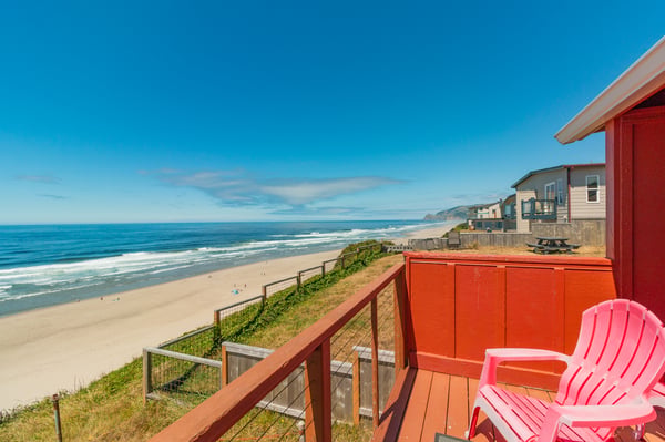 Bright coastal homes overlook a wide sandy beach and rolling waves under a clear blue sky, part of the surrounding neighborhood near this property.