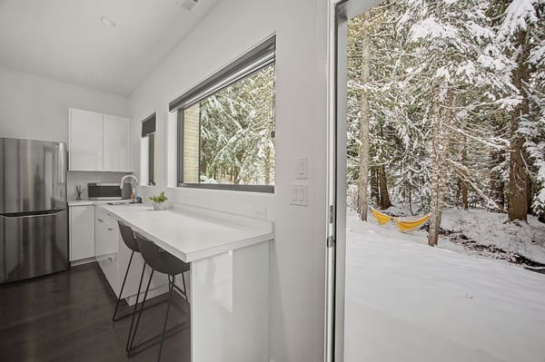 Your sleek kitchen opens to a winter wonderland, where snow-dusted trees create a magical backdrop for morning coffee.