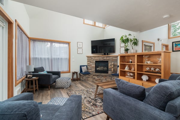 Relax in your spacious living room featuring a cozy stone fireplace, comfortable seating, and natural light from skylights above.