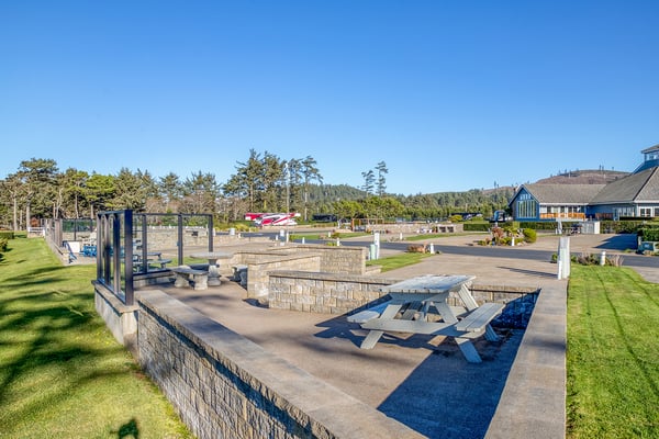 Spacious outdoor recreation area featuring picnic tables and BBQ facilities surrounded by coastal landscape and mountain views.