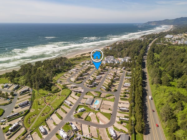 Aerial view showcasing a coastal vacation property nestled between forested hillsides and pristine ocean beaches, with direct access to scenic Oregon coastline.