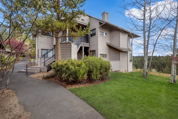 A modern two-story building nestled among towering pines and aspens, with a forested hillside backdrop visible from the property's landscaped grounds.