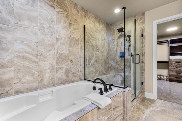 Relax in your luxurious spa-like bathroom featuring a deep soaking tub and spacious walk-in shower with dual showerheads, all finished in elegant travertine tile.