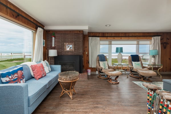 Unwind in your spacious coastal living room where sweeping ocean views frame your stay. Sink into comfortable seating by the fireplace and let the calming blues and warm wood tones wrap you in beachside tranquility.