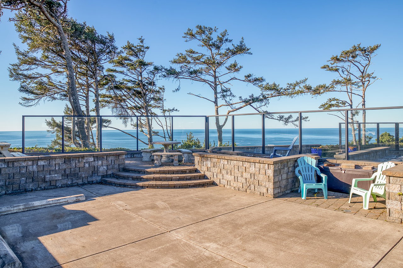 Oceanfront terrace with panoramic sea views through mature pines and glass railings.