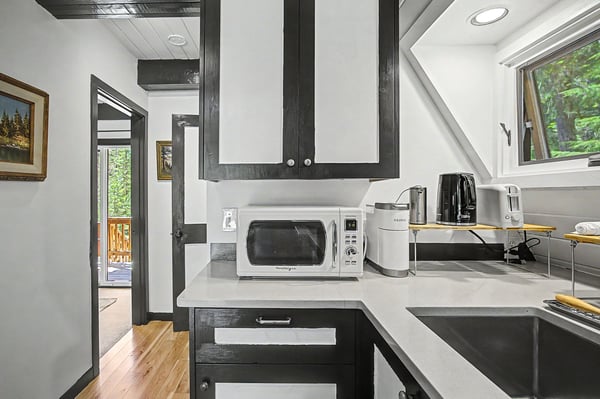 Your modern kitchen features sleek counters, a stocked microwave and coffee maker, and bright windows overlooking greenery—perfect for your morning routine or preparing a quick meal during your stay.