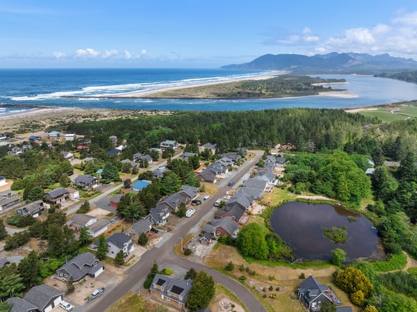 Aerial view of a coastal residential community nestled between forested hills, sandy beaches, and mountain vistas, offering serene natural surroundings and oceanfront access.