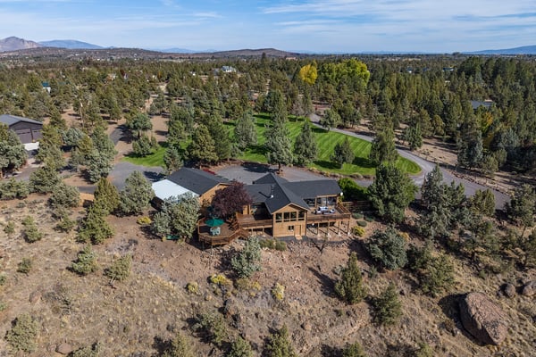 Aerial view of a charming wood-sided vacation home nestled among trees in a peaceful, scenic neighborhood with mountain vistas.