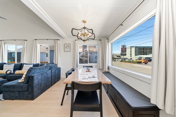 Gather around the live-edge table in this airy open-concept space, where natural light floods through floor-to-ceiling windows and vaulted ceilings create an inviting atmosphere for your coastal getaway.