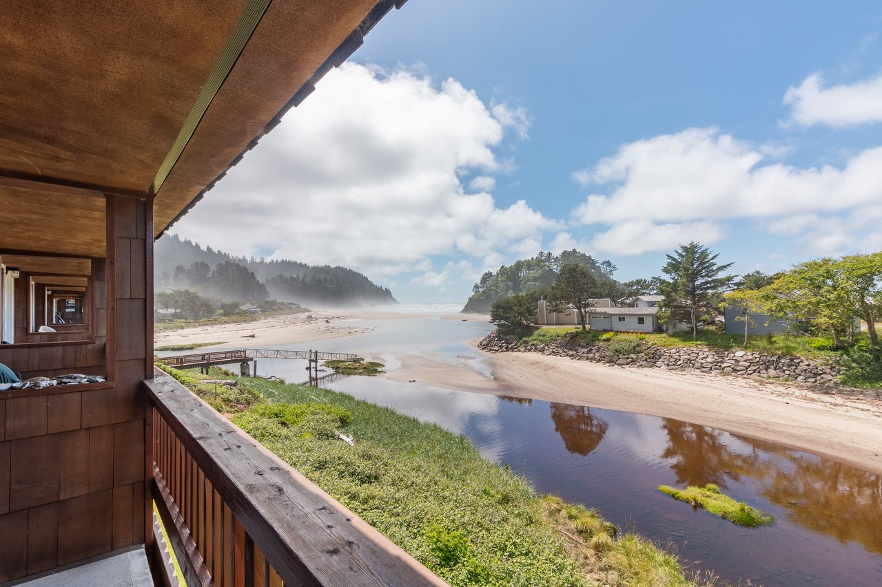 Coastal property overlooking a serene river meeting the Pacific Ocean, with forested hillsides and sandy beaches defining the scenic surrounding area.