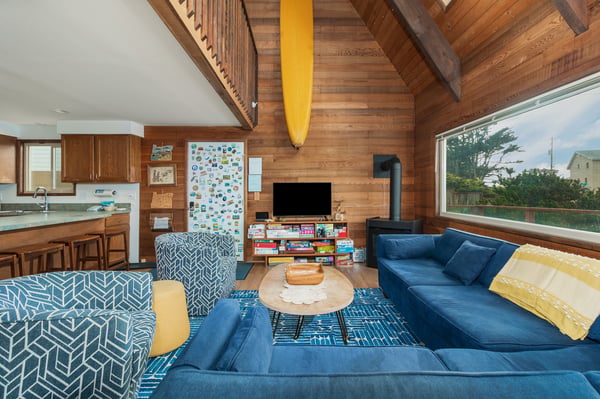 Relax in your cozy coastal living room with soaring wood ceilings, plush blue seating, and a crackling fireplace—perfect for unwinding after beach days.