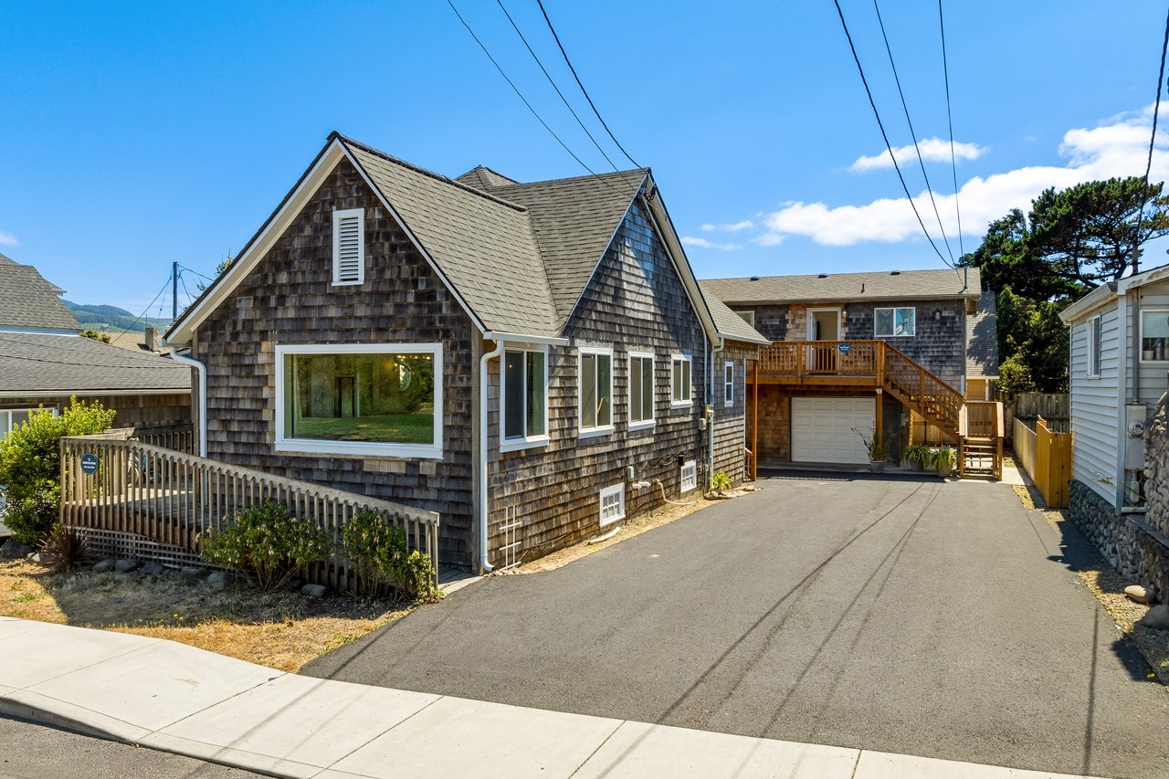 A classic coastal cottage with weathered shingle siding and mountain backdrop, situated in a quiet residential neighborhood with parking and outdoor deck access.
