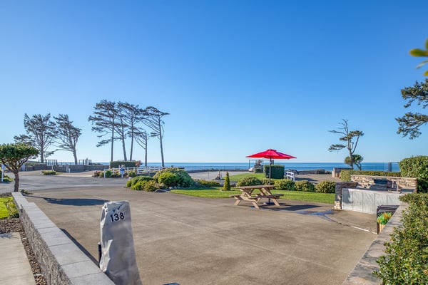 Expansive oceanfront setting with coastal trees and blue skies, featuring outdoor seating areas and direct beach access.