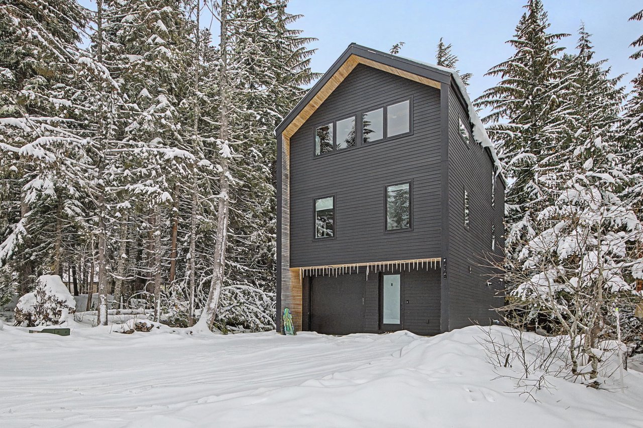Modern mountain retreat nestled among snow-laden evergreens in pristine winter wonderland.