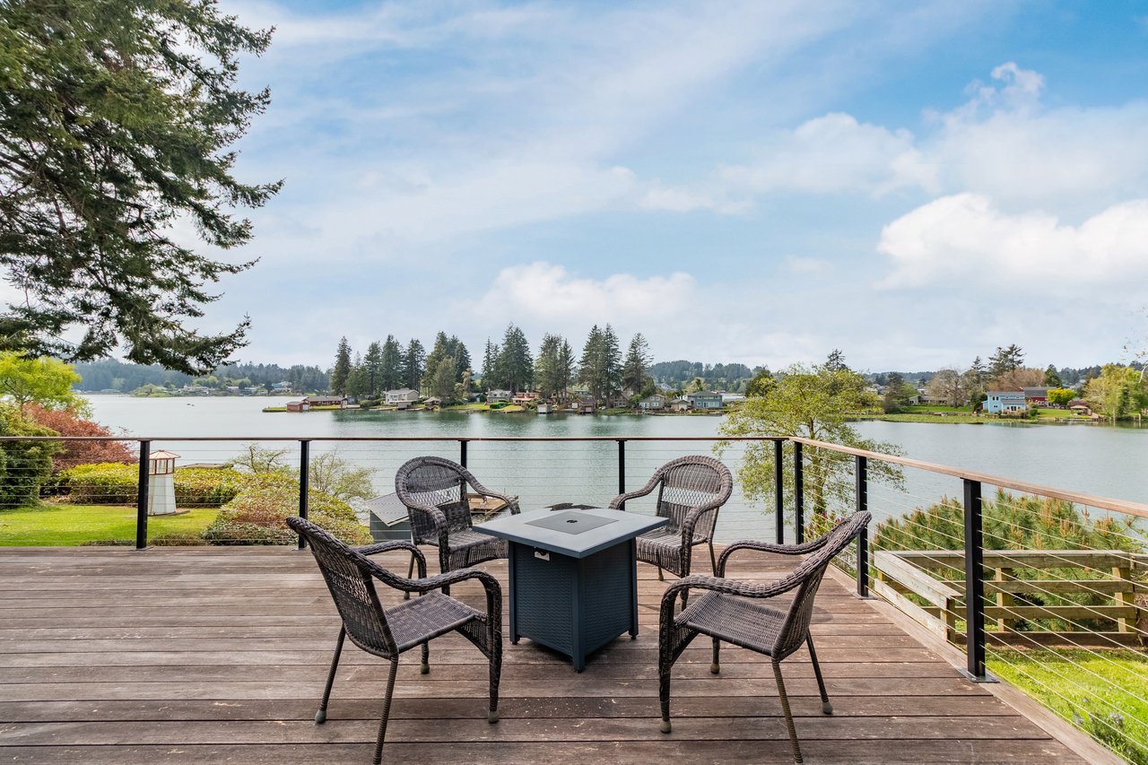 Spacious waterfront deck overlooks serene lake views, framed by evergreens and distant shoreline. A peaceful setting with comfortable seating invites you to relax and unwind.