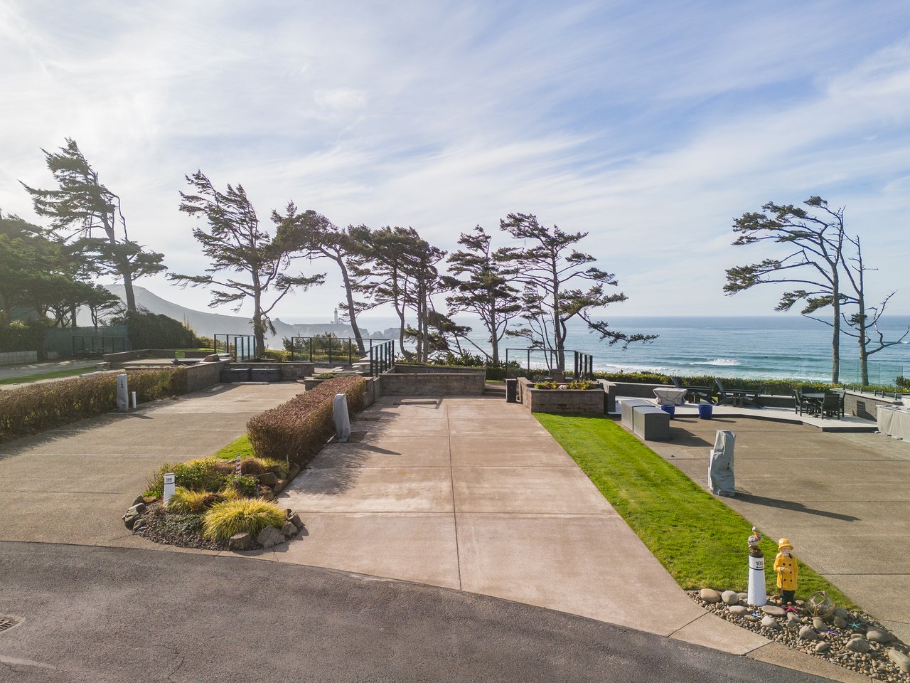 A coastal property featuring landscaped pathways, manicured lawns, and dramatic wind-sculpted pines along the ocean's edge.