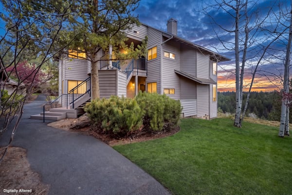 A welcoming two-story vacation home nestled among evergreens with a glowing sunset backdrop and manicured lawn, perfect for a peaceful mountain retreat.
