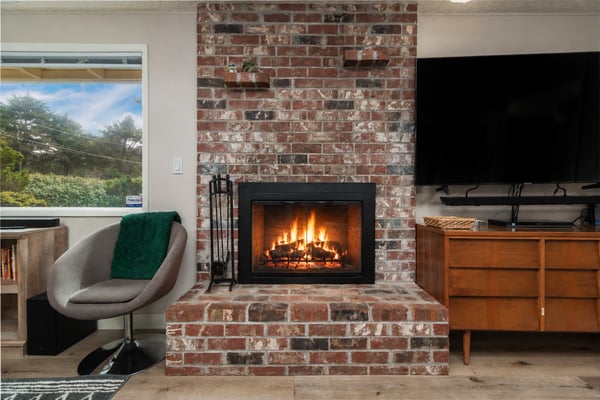 Warm up by your own crackling fireplace beneath the rustic brick, with lush green views through the window and a cozy spot to unwind.