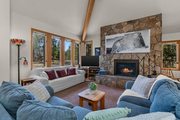 Sink into plush seating by your crackling stone fireplace as natural light floods this inviting living space through panoramic windows.
