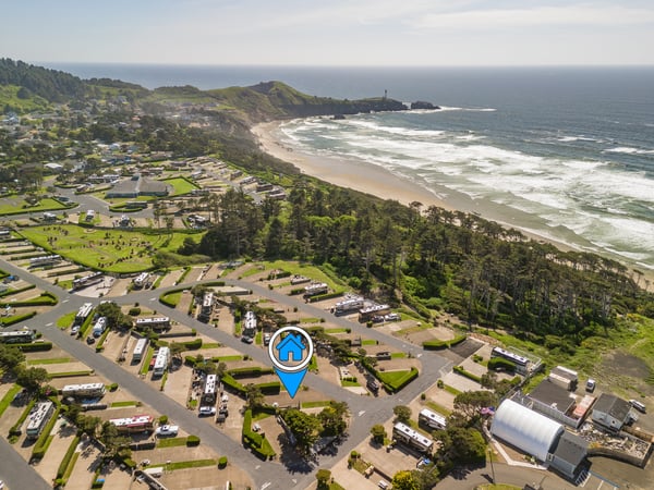 Aerial view of a coastal property nestled between rolling green hills and pristine sandy beach, with a lighthouse marking the scenic headland and ocean waves beyond.