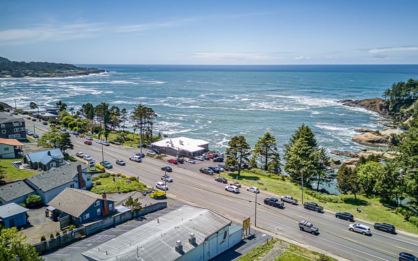 Aerial view of the coastal property area, showing its scenic location along the Pacific shoreline, with easy road access and surrounding neighborhood positioned between ocean vistas and natural headlands.