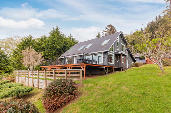 Modern hillside rental with spacious deck, surrounded by lush landscaping and mature trees in a quiet natural setting.