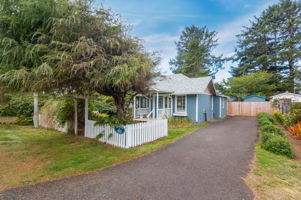 Charming coastal cottage with white picket fence and mature trees, set in a peaceful neighborhood near the coast.