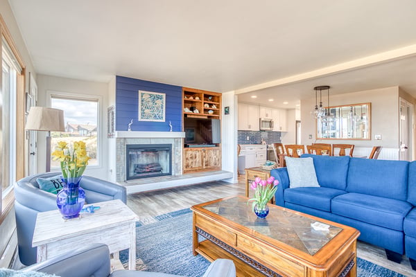 Relax by your cozy fireplace in this bright, open living space where blue accents and warm wood create the perfect retreat atmosphere.