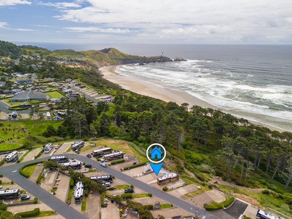 Aerial view of a coastal property nestled between lush green hills and a pristine sandy beach, with a lighthouse marking the scenic headland and ocean waves rolling in.