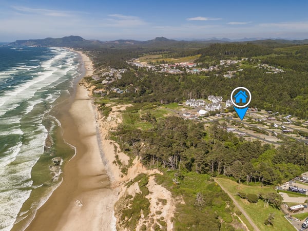 Aerial view of a coastal property nestled among lush forests, with pristine beaches and mountain ranges defining the stunning natural landscape of the surrounding area.