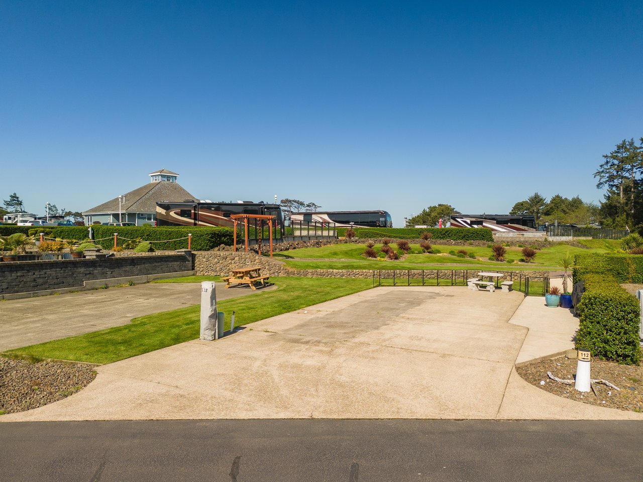 The property features a spacious lawn with picnic areas, landscaped gardens, and a pergola, all set within a well-maintained resort community under clear skies.