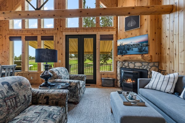 Sink into plush seating as the fireplace glows warmly before you. Soaring timber beams and sweeping views across the greens invite you to unwind in this serene, light-filled haven.