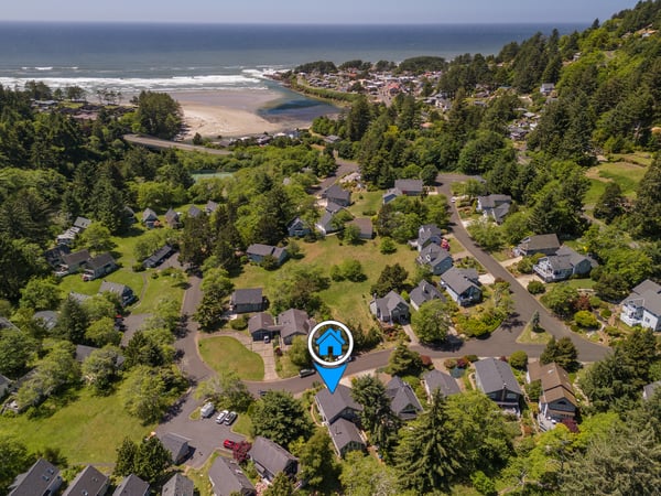 Aerial view of a coastal neighborhood nestled among trees, with beach access and ocean views in a peaceful residential setting.