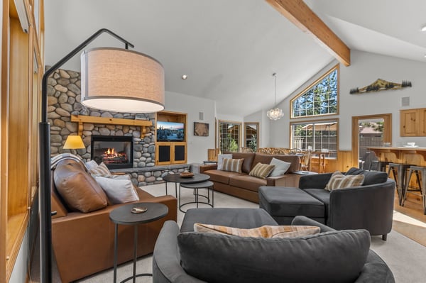 Sink into plush seating by the crackling stone fireplace as warm light fills the vaulted space, blending modern comfort with rustic mountain charm for your perfect retreat.