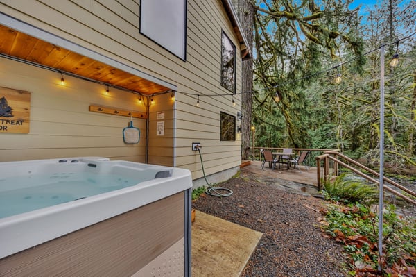Soak your cares away in your private hot tub, nestled beneath towering evergreens and soft string lights, with a peaceful forest backdrop all around.