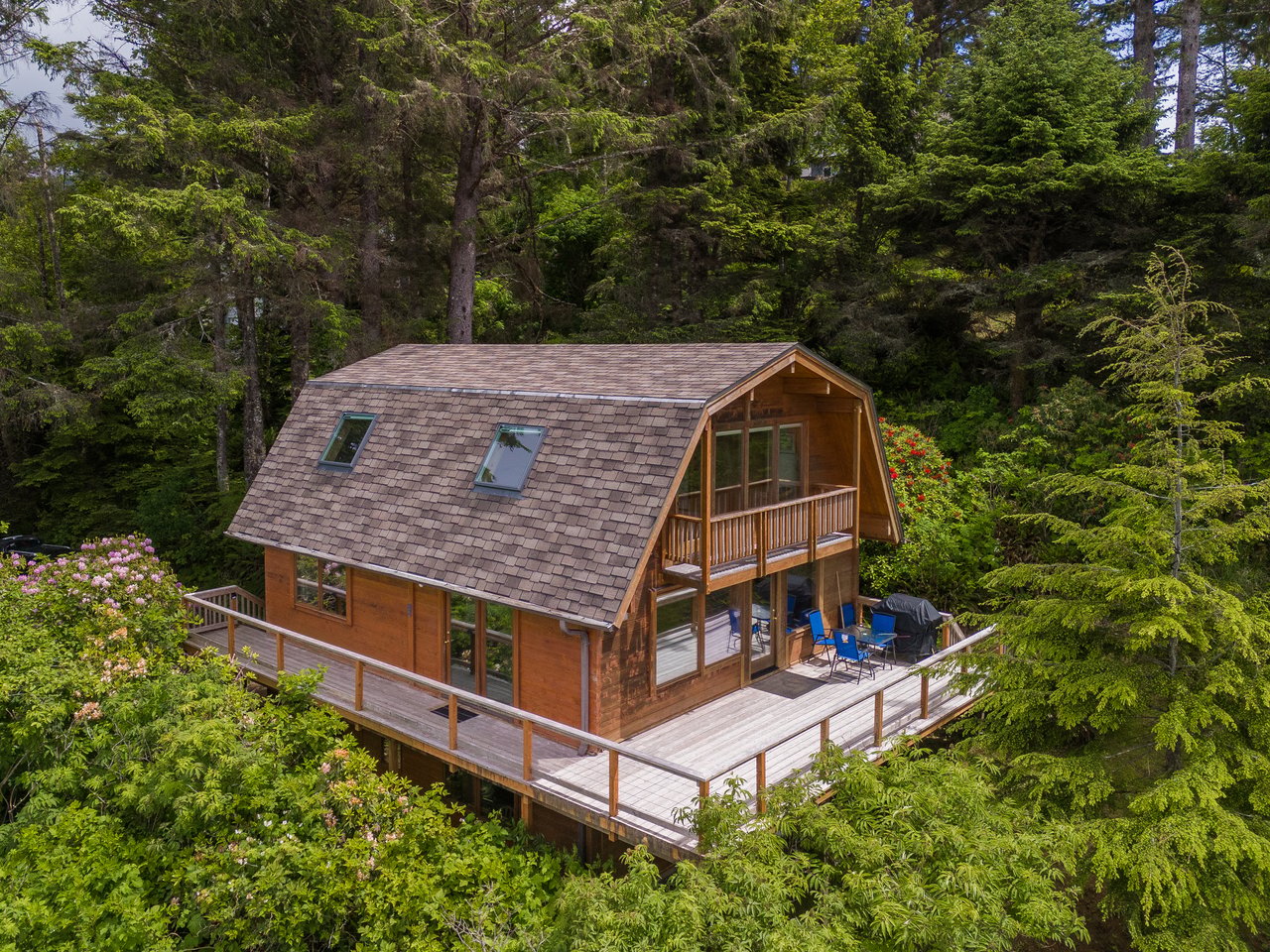 Charming cabin nestled in a lush forest setting, featuring spacious wrap-around deck and classic barn-style architecture surrounded by towering evergreens.