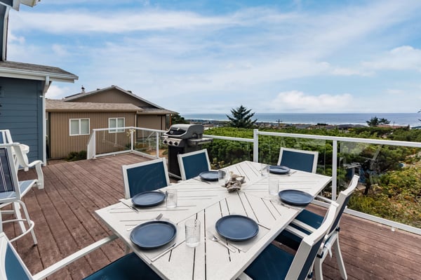 Property features a private deck with alfresco dining and BBQ facilities, set against coastal surroundings and neighboring residences.