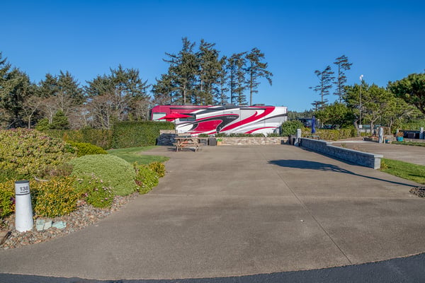 RV site with concrete pad and hookups surrounded by mature trees and manicured landscaping in a peaceful campground setting.