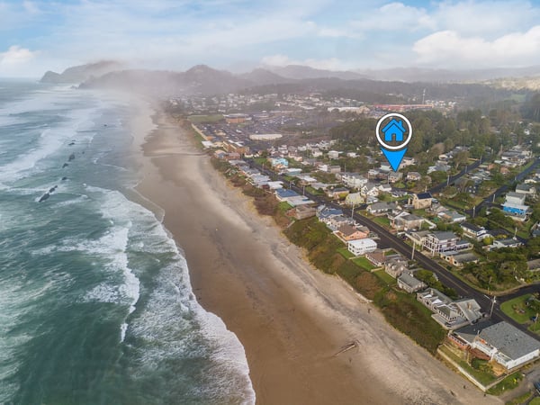 Stunning aerial view of coastal town with pristine beach stretching along dramatic Pacific coastline and forested mountains.