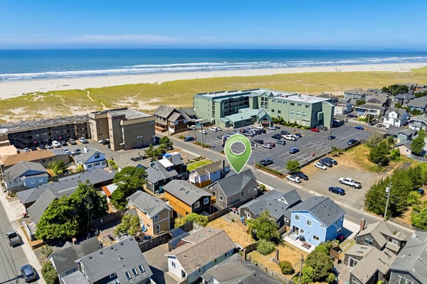 An aerial perspective reveals the property's prime location within a peaceful coastal neighborhood, just steps from the sandy shoreline and ocean waves.