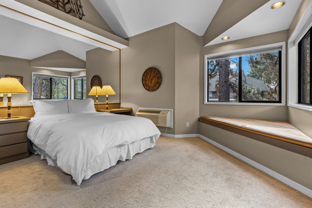 Unwind in your serene bedroom featuring vaulted ceilings, plush bedding, and a cozy window seat overlooking peaceful trees.