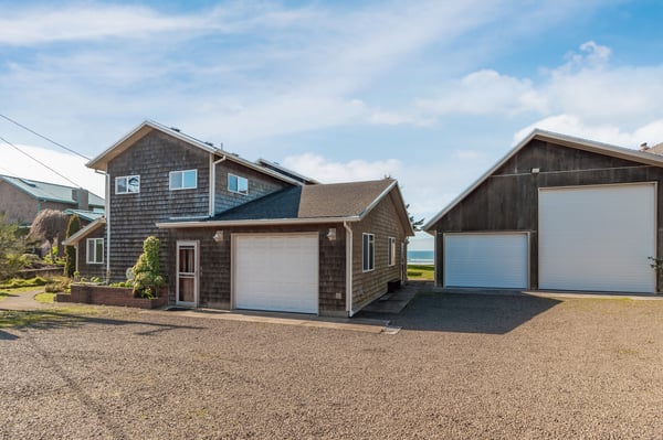 Coastal property with weathered shingle siding and multiple garage spaces, located near the ocean.