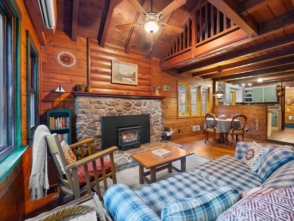 Cozy up in this rustic living room where exposed beams, stone fireplace, and plaid furnishings create your perfect mountain retreat atmosphere.